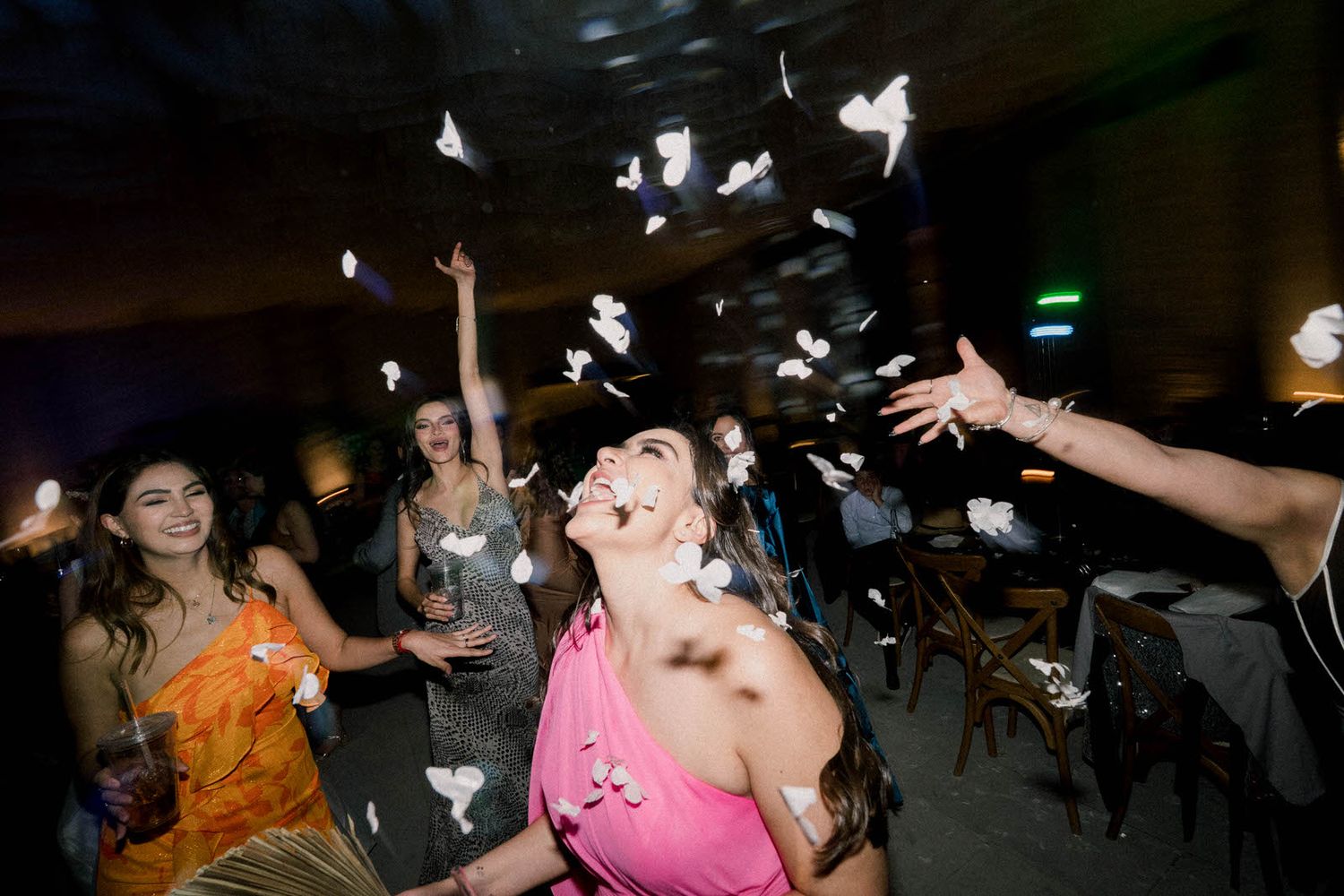Party guests celebrate with flying confetti under dramatic lighting.