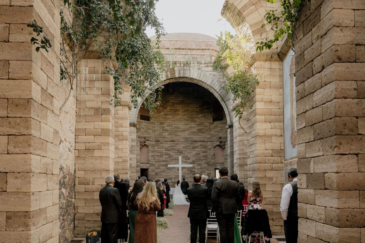 A stone church courtyard with arched columns and greenery during a wedding ceremony.