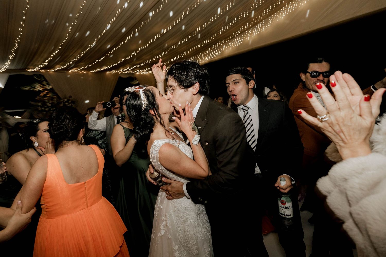 Wedding party dances beneath elegant white draped ceiling with sparkling lights.