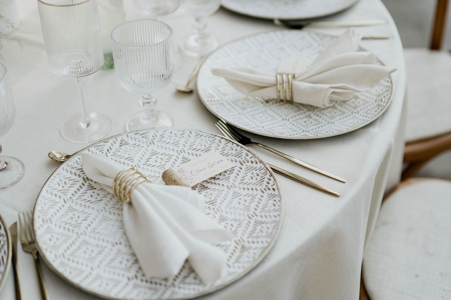 White place settings with delicate bow details and textured charger plates on an elegant dining table.