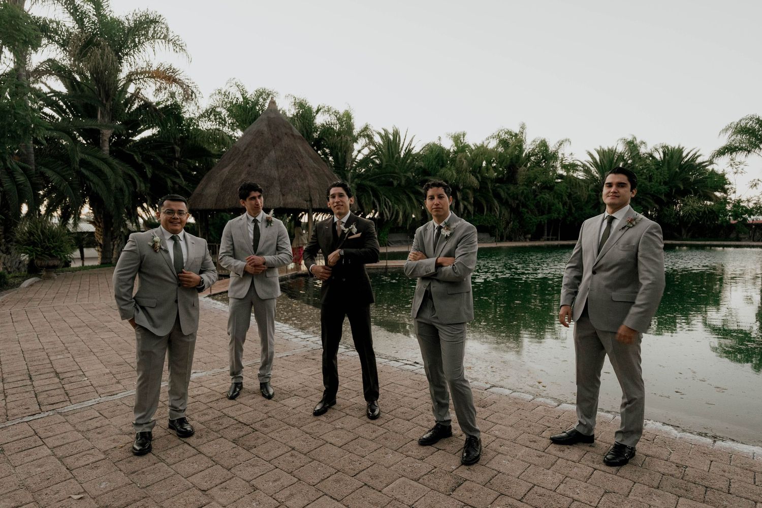 Wedding party members in formal attire pose along a waterfront walkway.