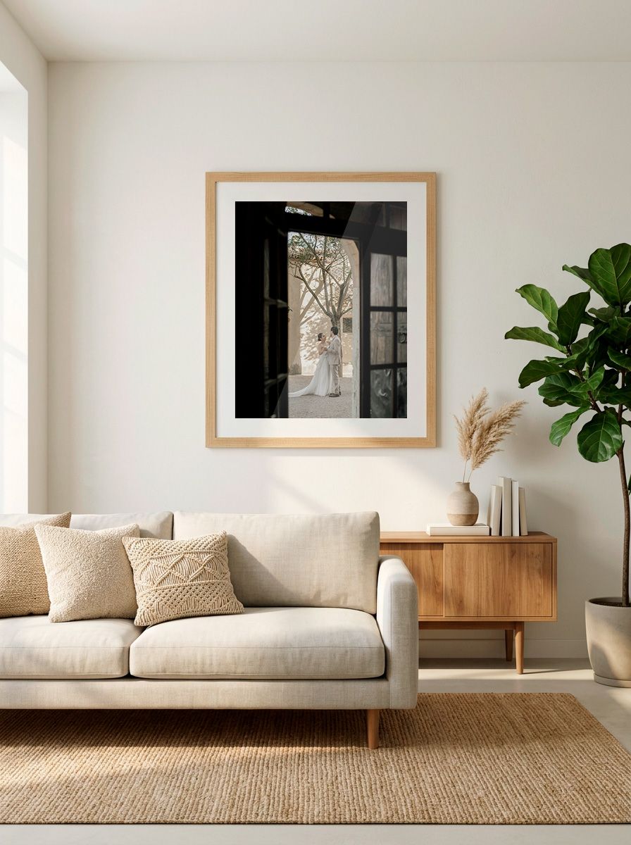 Minimalist living room with beige sofa, wooden sideboard, fiddle leaf fig, and framed botanical art print on white wall.
