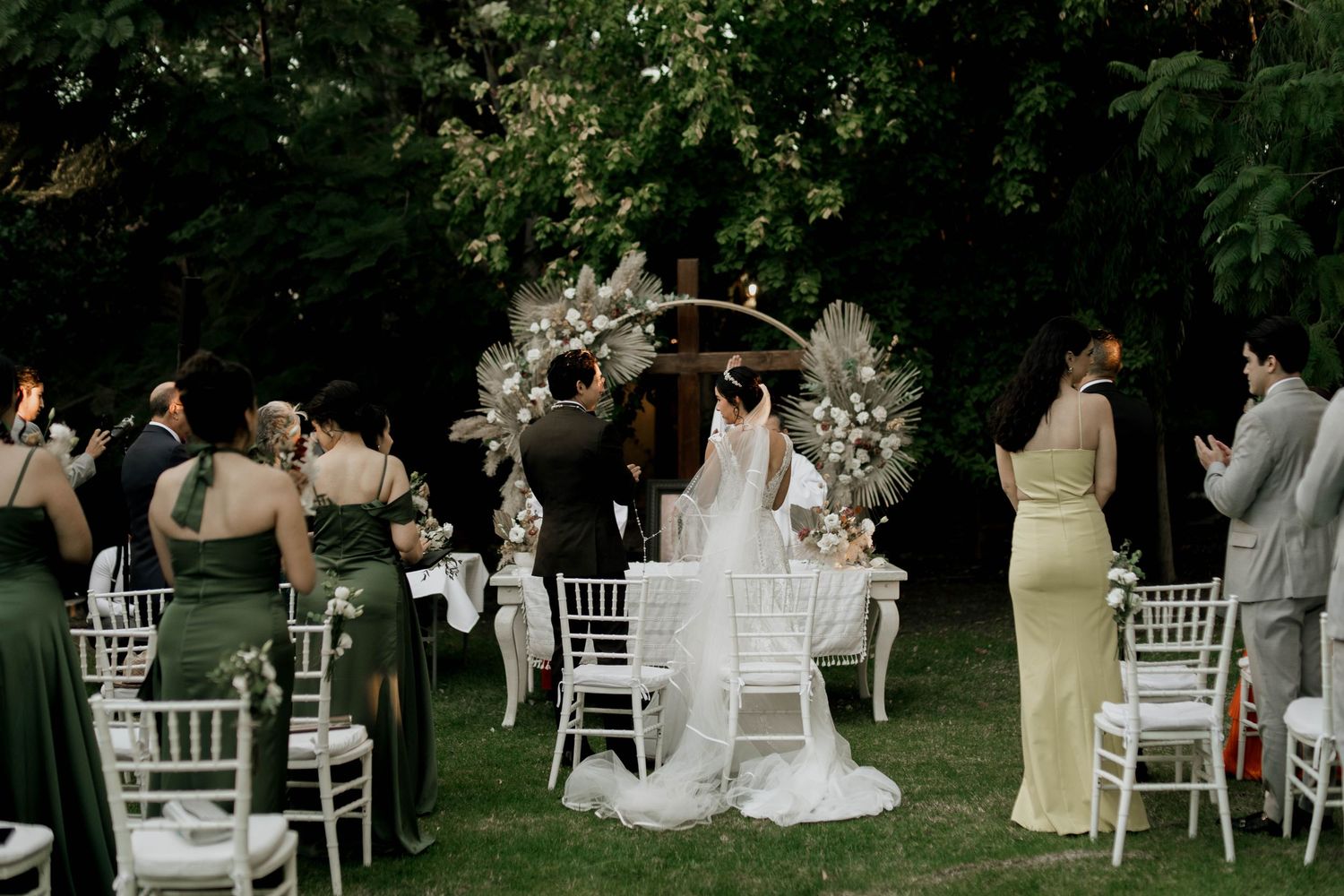 Outdoor wedding reception setup with white chiavari chairs arranged on a green lawn.