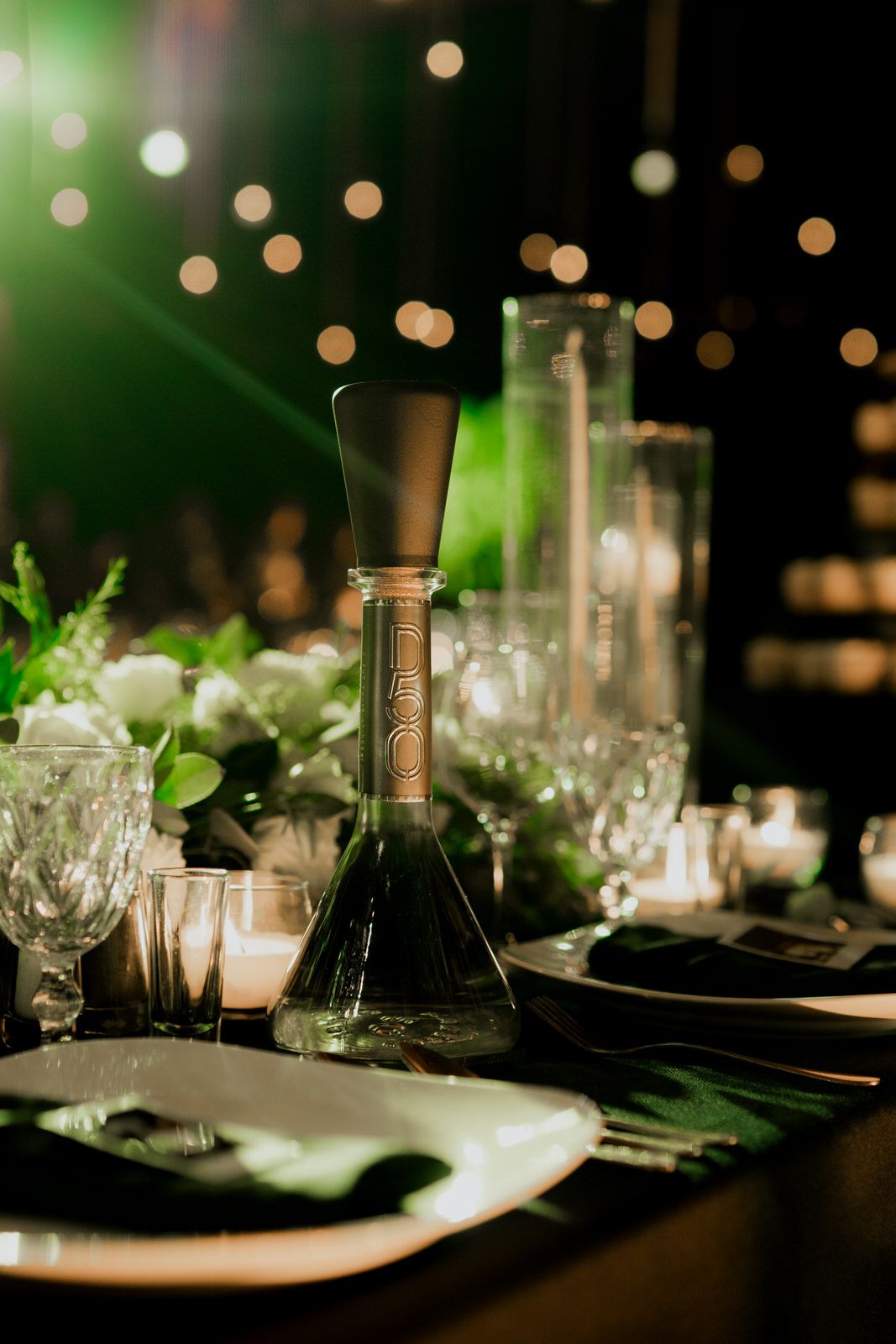 Intimate table setting with wine bottles and crystal glasses under ambient lighting.
