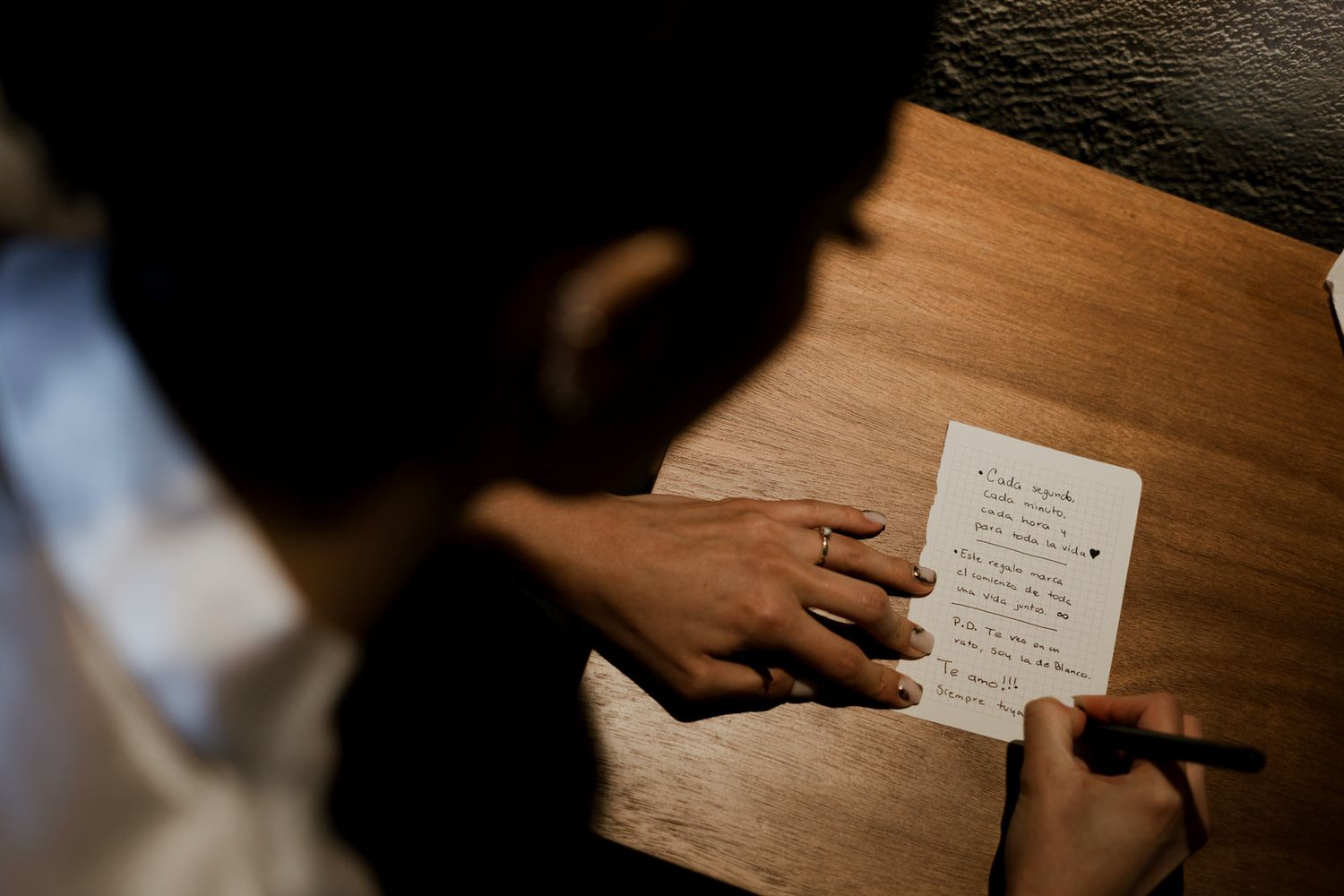 Dark wooden table with hands visible reaching for paper documents in dim lighting.