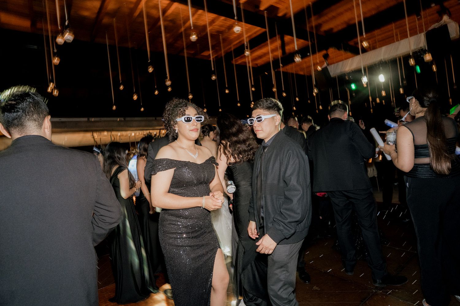 Party guests dancing and mingling at a dimly lit indoor event venue with hanging lights.