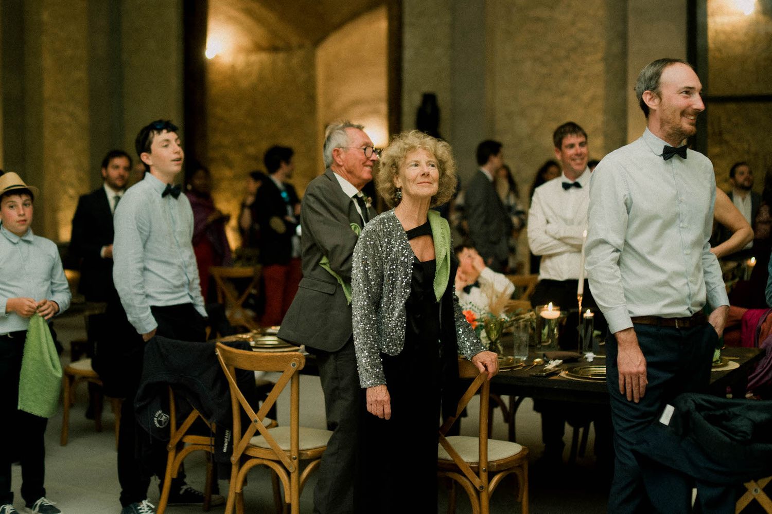 Panoramic view of wedding guests mingling during evening reception in stone-walled venue.