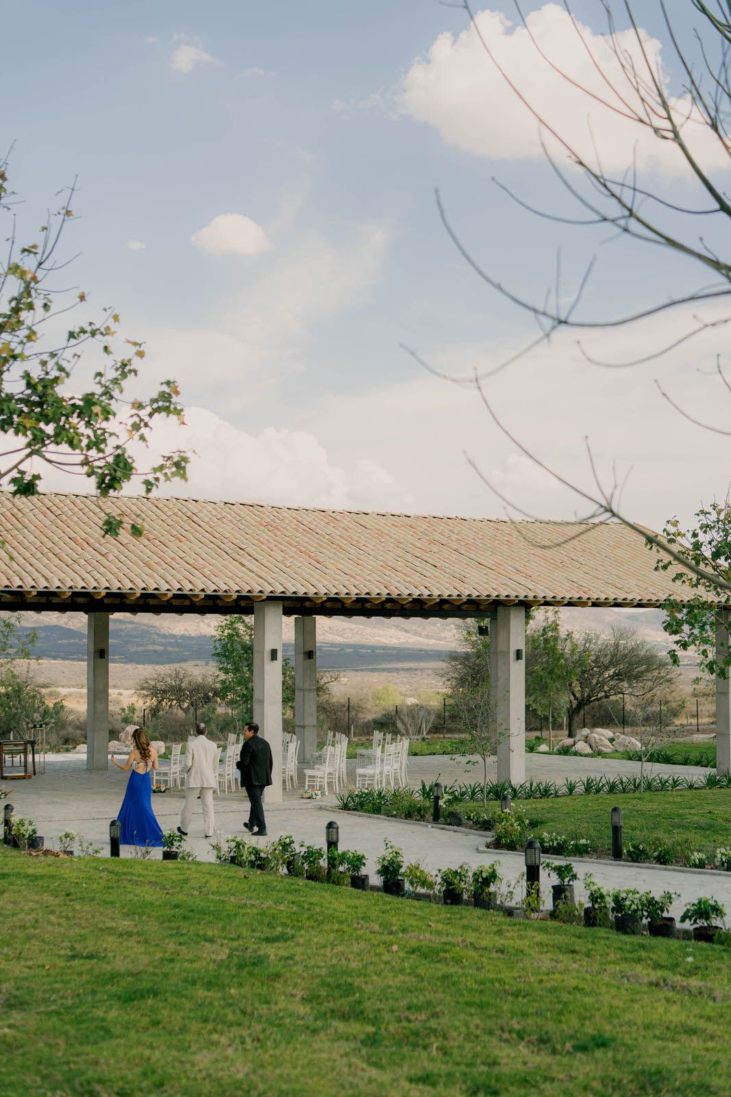 A covered outdoor pavilion with white columns stands in a landscaped garden setting.