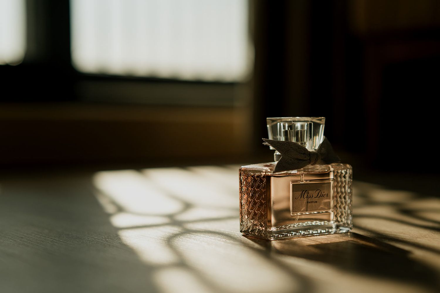 Elegant glass perfume bottle with golden hue sitting on a surface bathed in warm sunlight and geometric shadows.