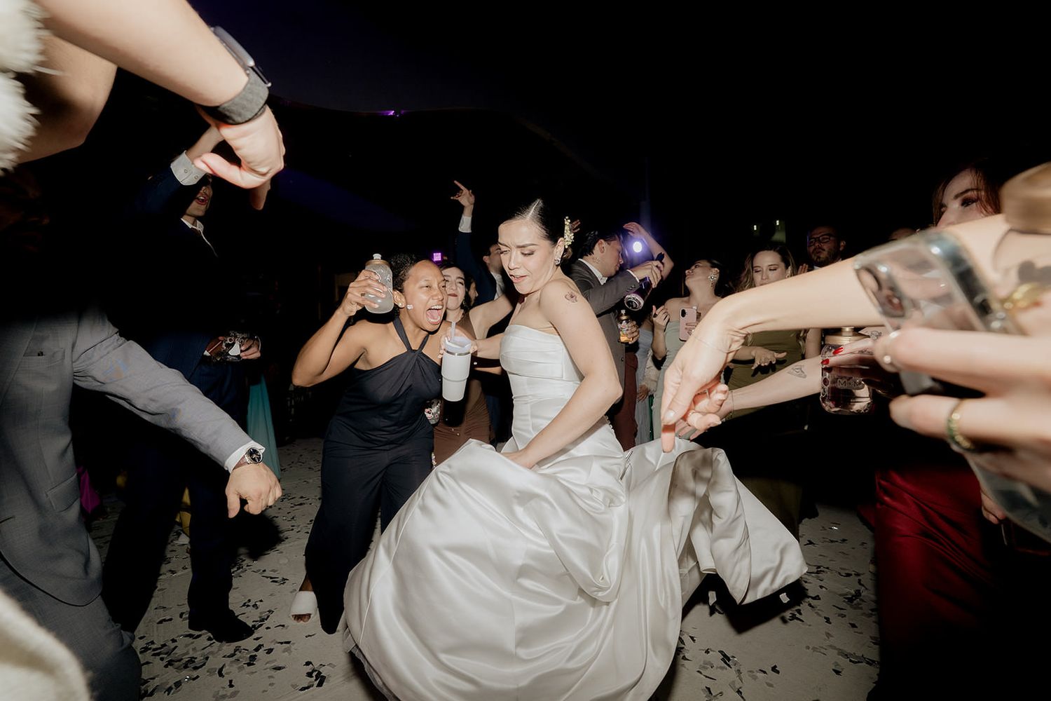 Bride in white gown dancing joyfully with guests at a lively wedding reception celebration.