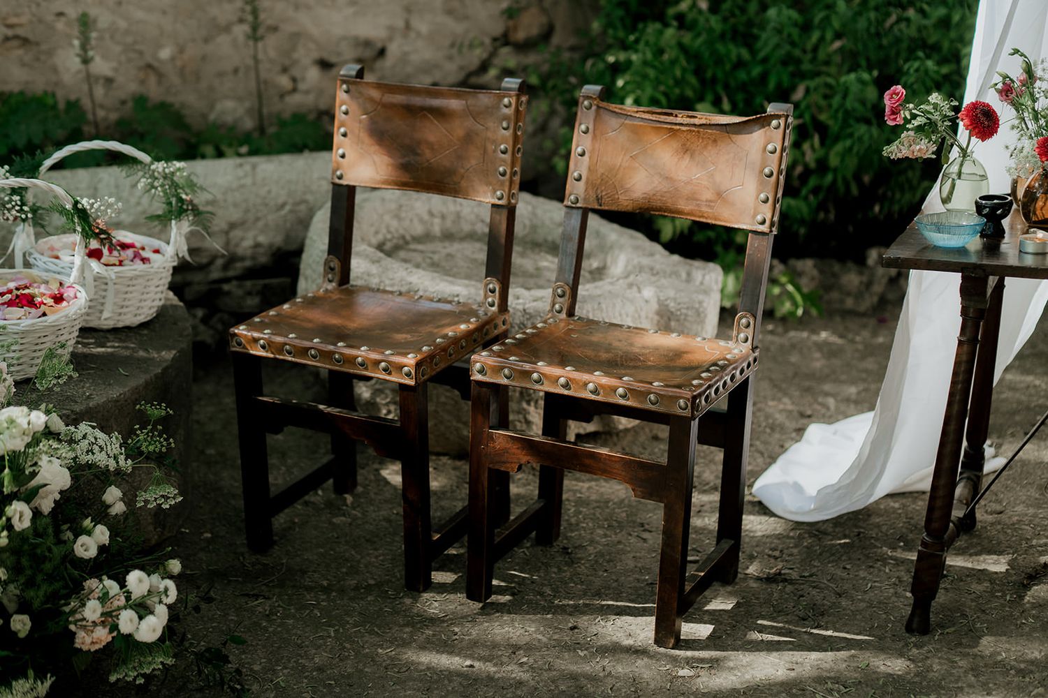 A rustic outdoor seating arrangement with vintage wooden chairs and blooming white flowers in a garden setting.