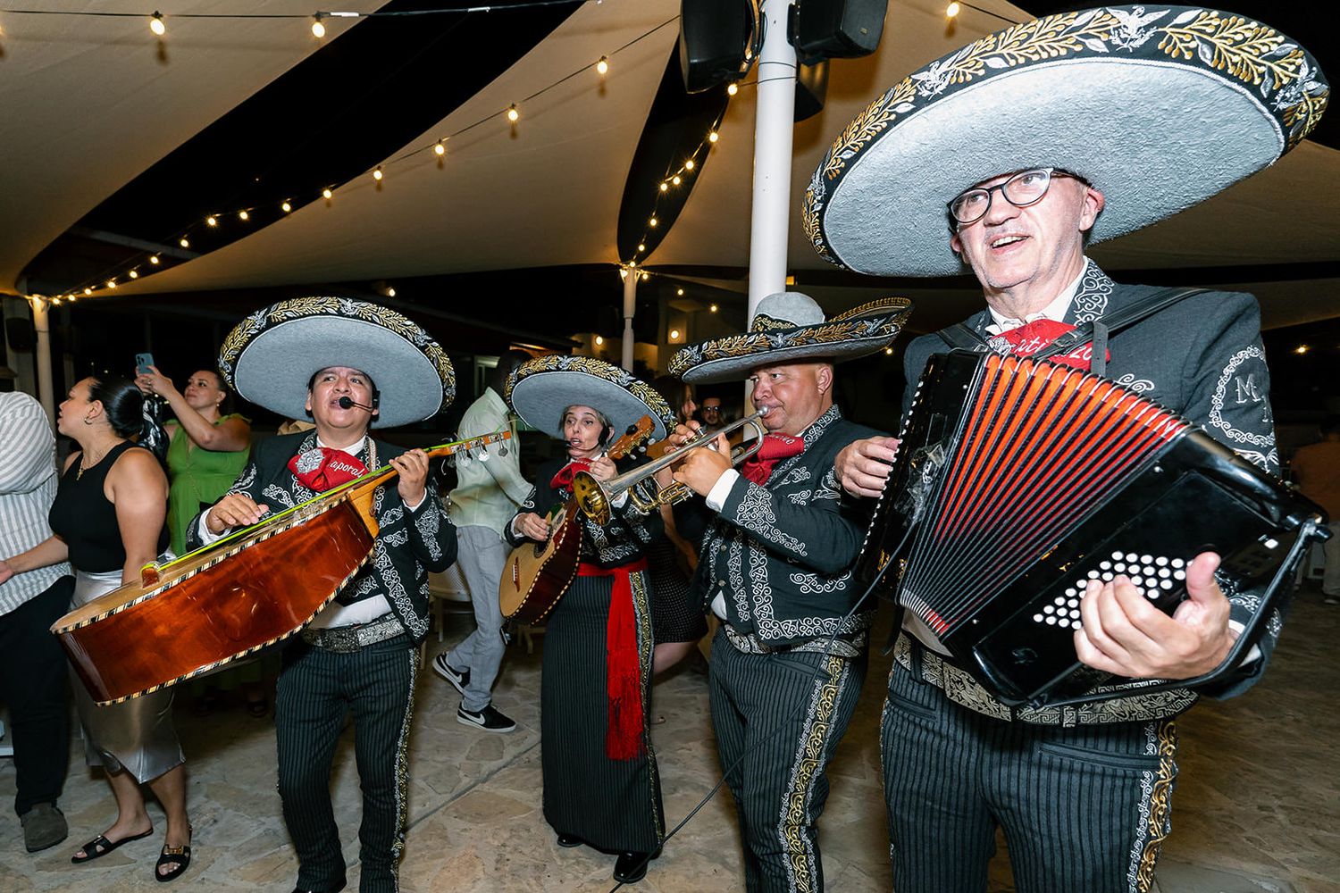 Musicians performing with traditional instruments at an outdoor celebration under string lights.