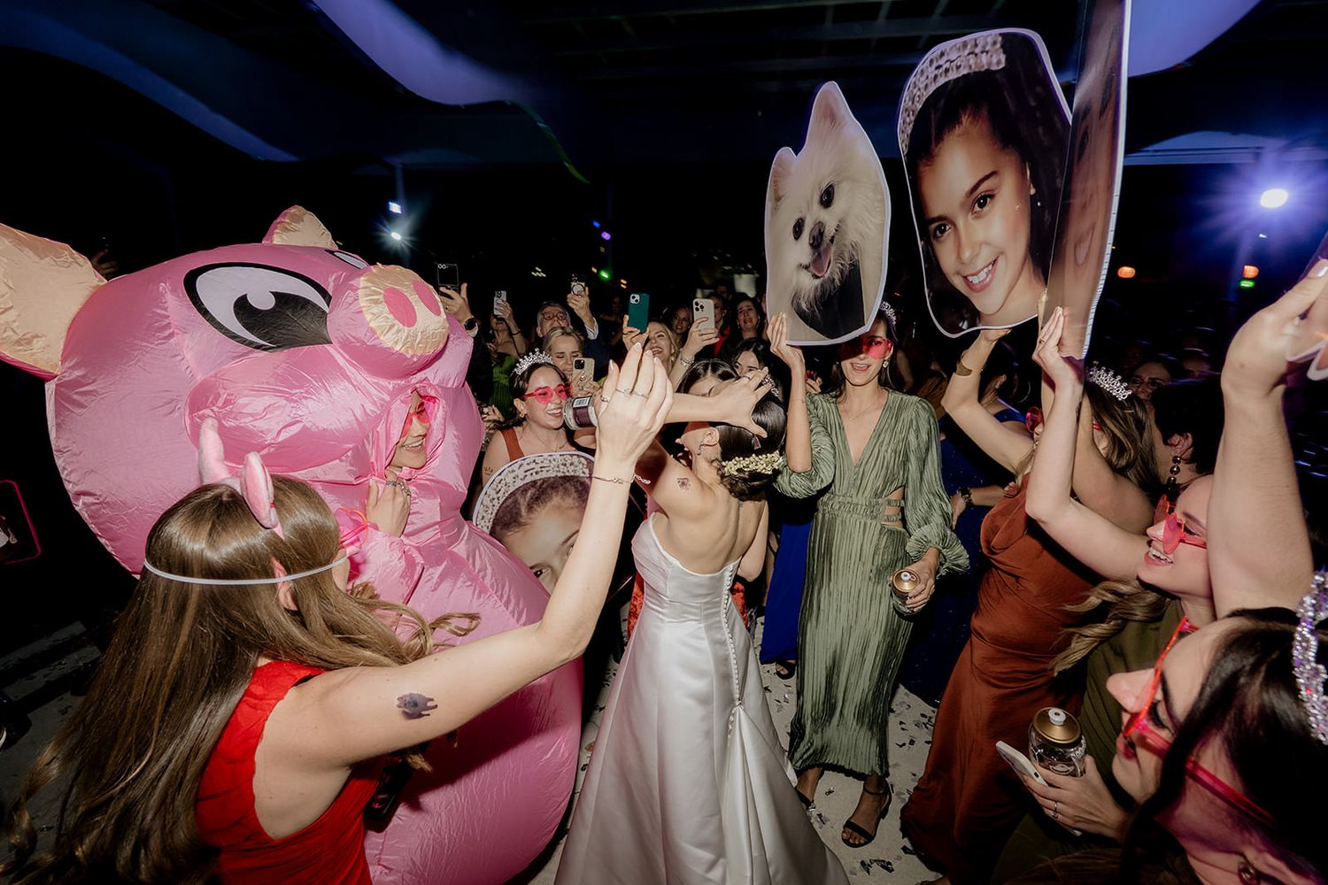 Bride surrounded by guests holding inflatable pig and photo cutout at wedding reception.