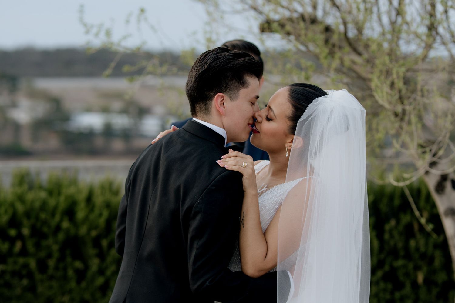 Newlywed couple shares romantic first kiss outdoors with scenic landscape in the background.
