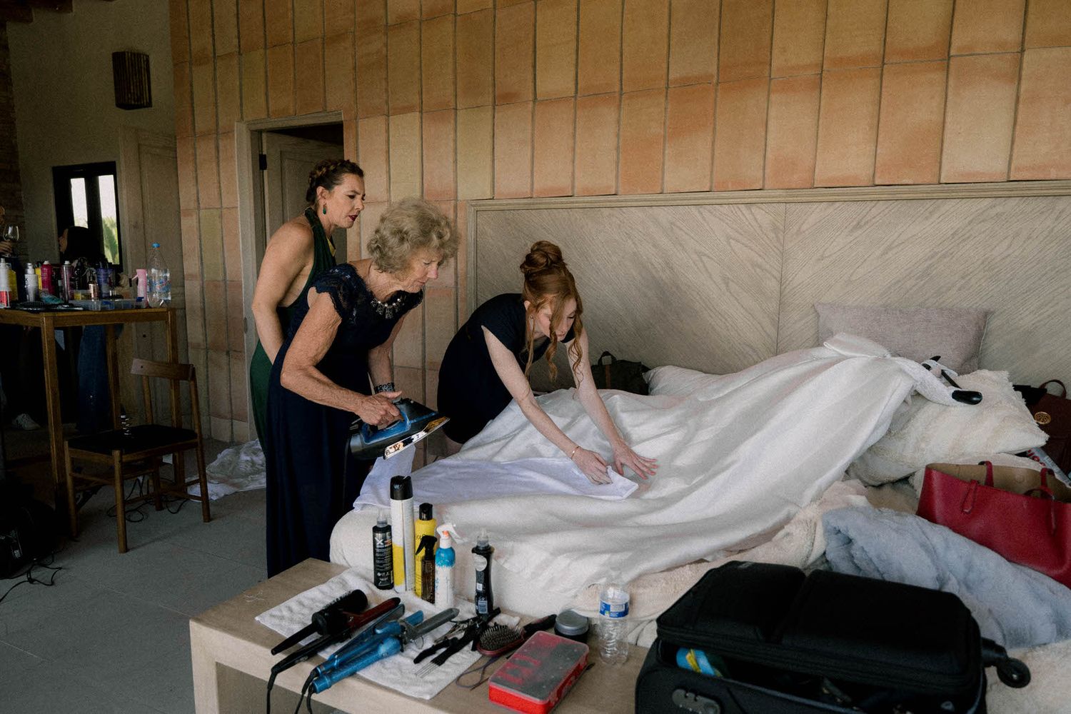 People ironing and steaming white fabric on a table in a room with brick walls.