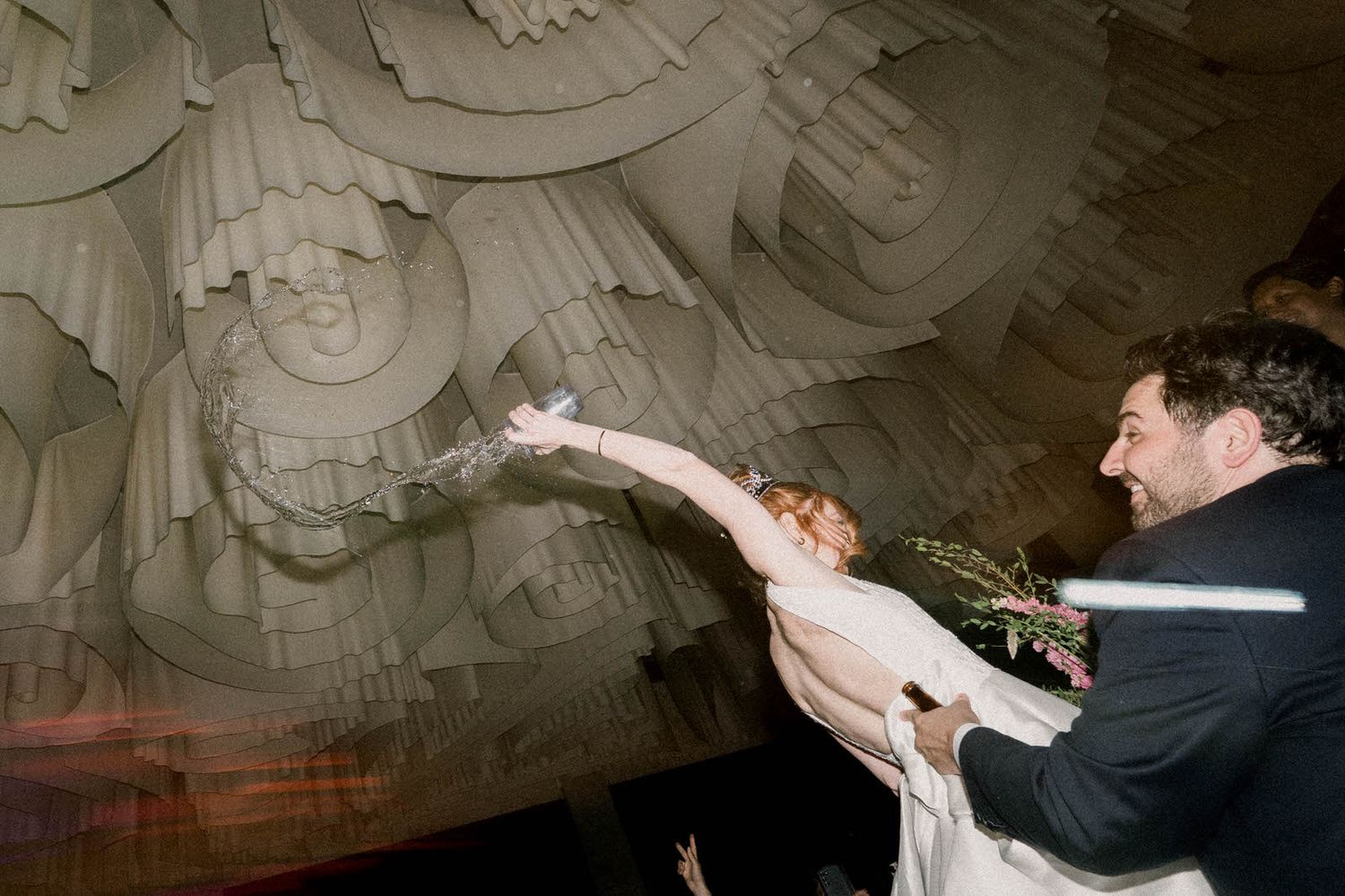 Wedding guests celebrate beneath an intricately designed ceiling at an elegant venue.