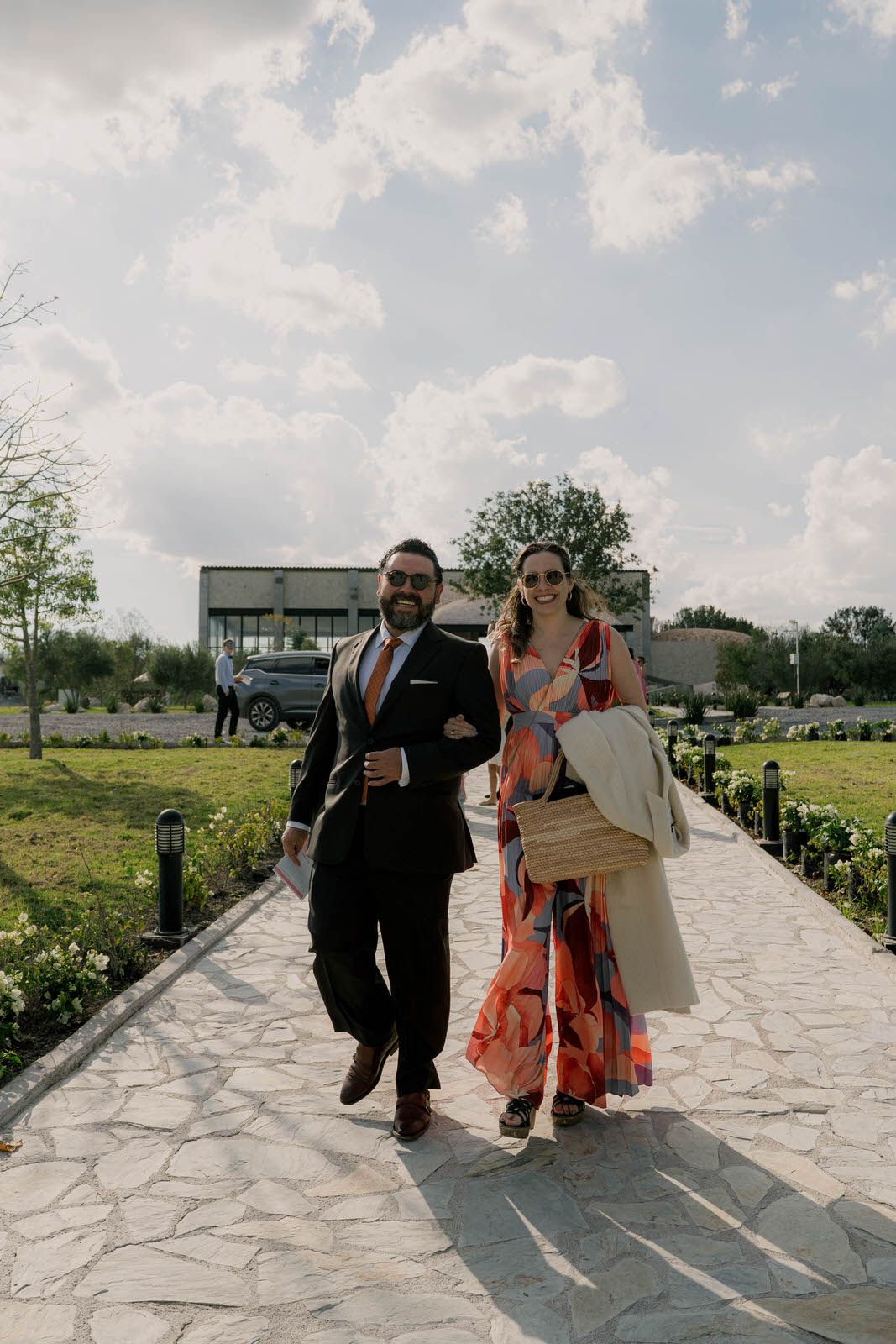 Wedding guests walk along a stone path under bright blue skies at an outdoor venue.