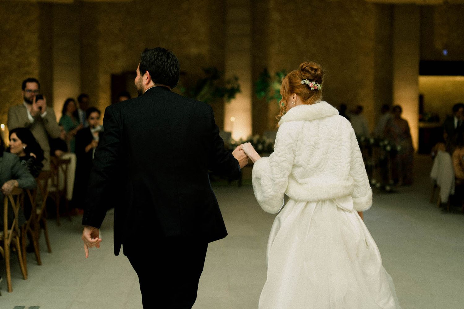 Couple sharing first dance at wedding reception with guests watching from sides.