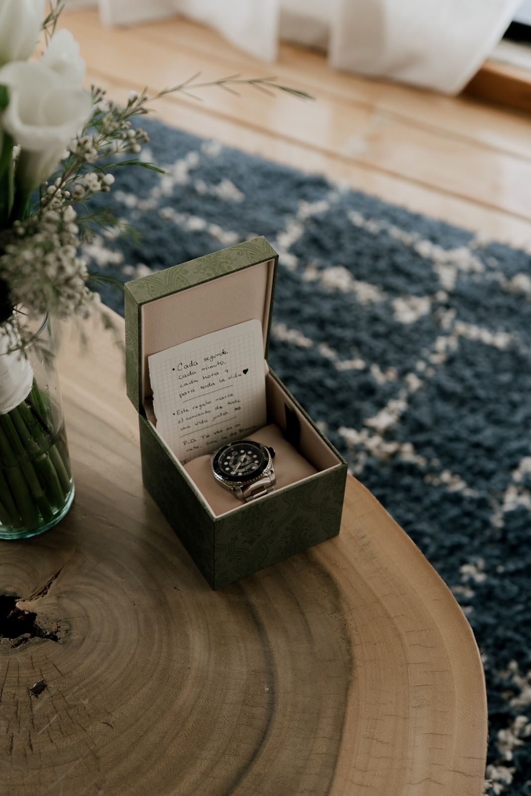 Watch gift box with handwritten note displayed on wooden tree trunk slice table.