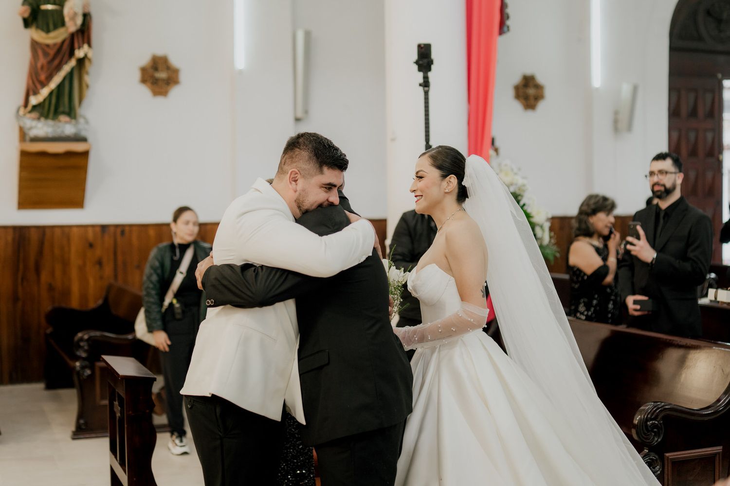 A tender moment during a Catholic church wedding ceremony with a couple embracing in front of wooden pews.