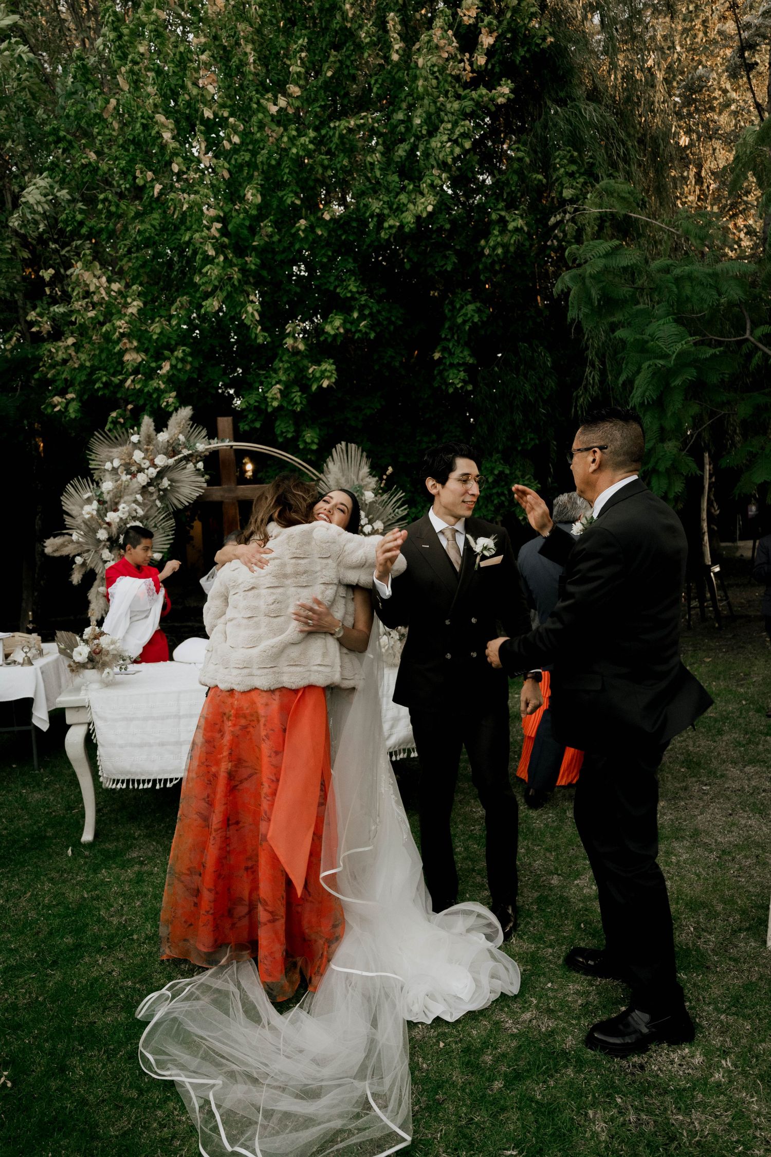Wedding celebration with guests in formal wear and bright orange dresses at an outdoor venue.