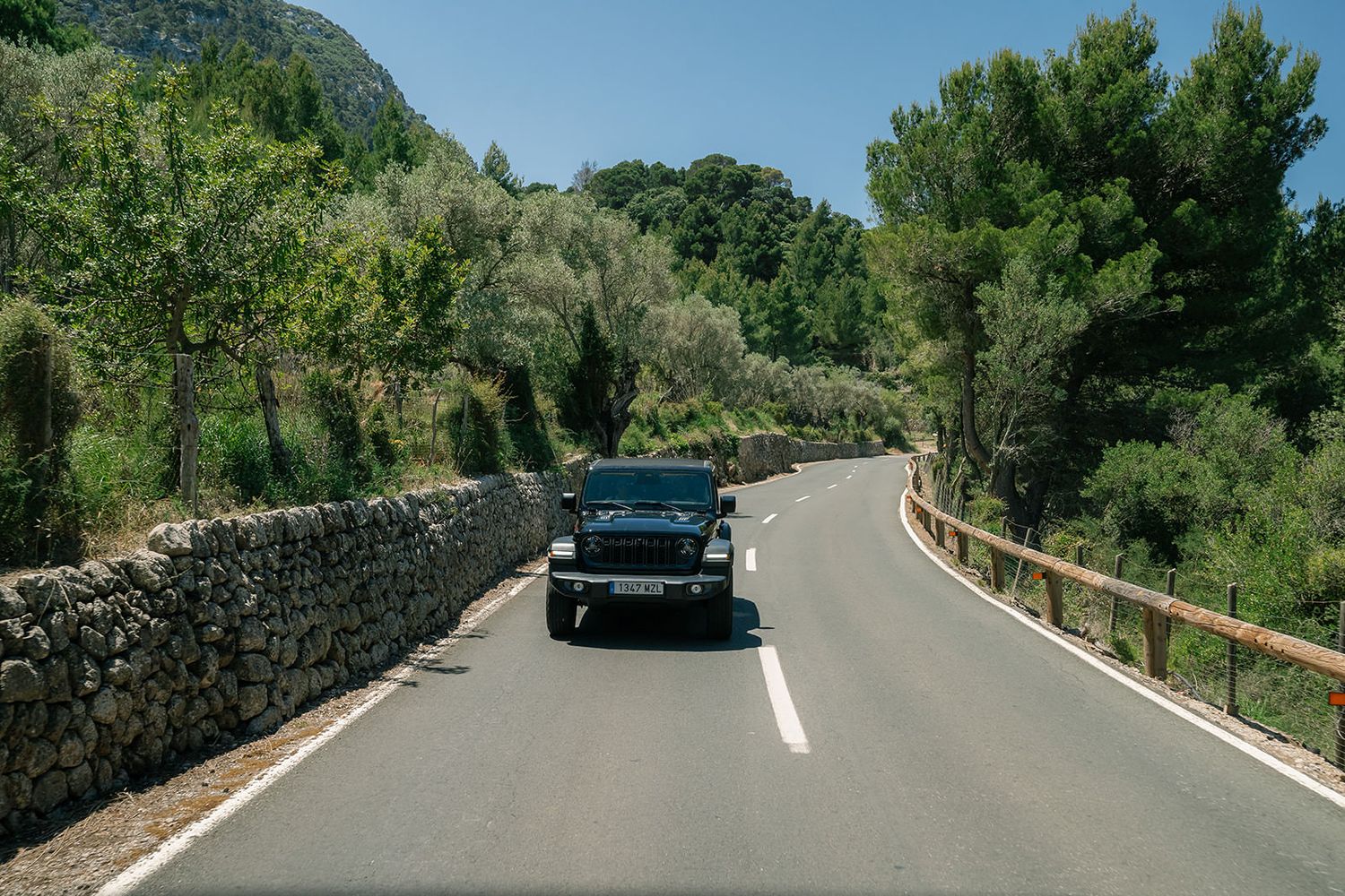 Scenic winding mountain road with stone walls and lush greenery along the curves.