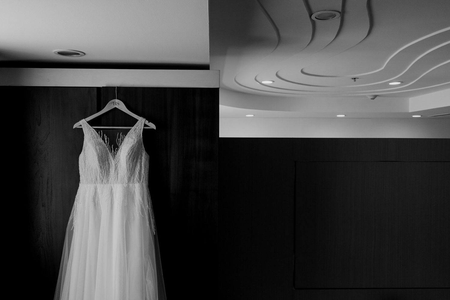 Elegant white wedding dress hanging on a hanger in a dark room, black and white photography.