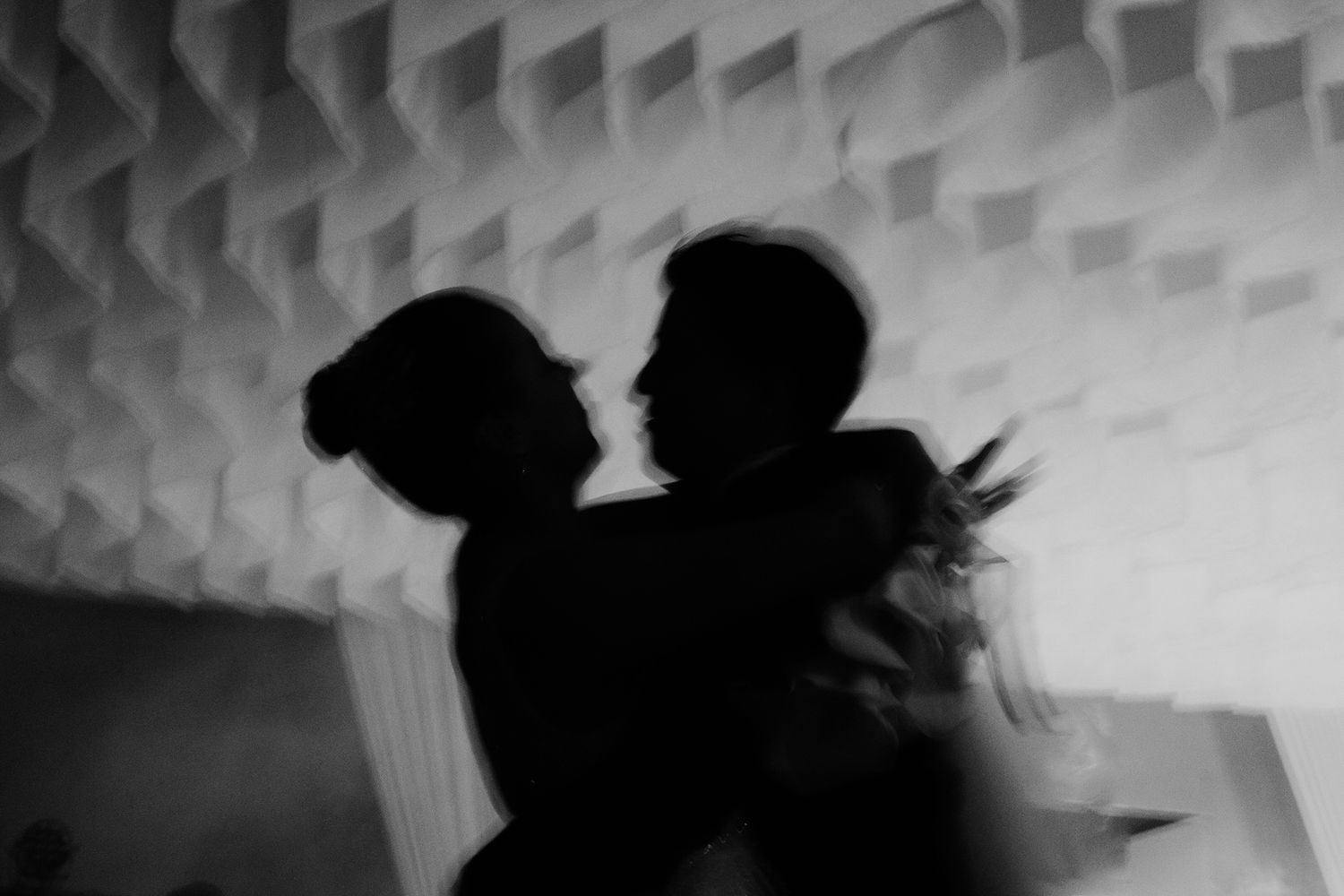 Artistic black and white silhouette of bride and groom dancing closely together at their wedding reception.