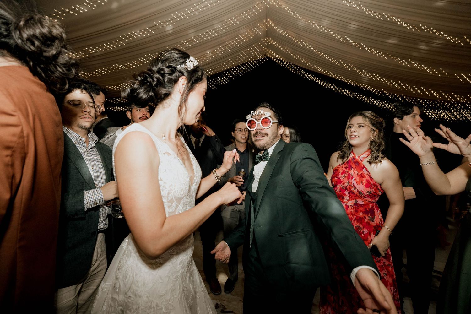 Energetic dance party at wedding reception with guests dancing beneath draped ceiling decorations.