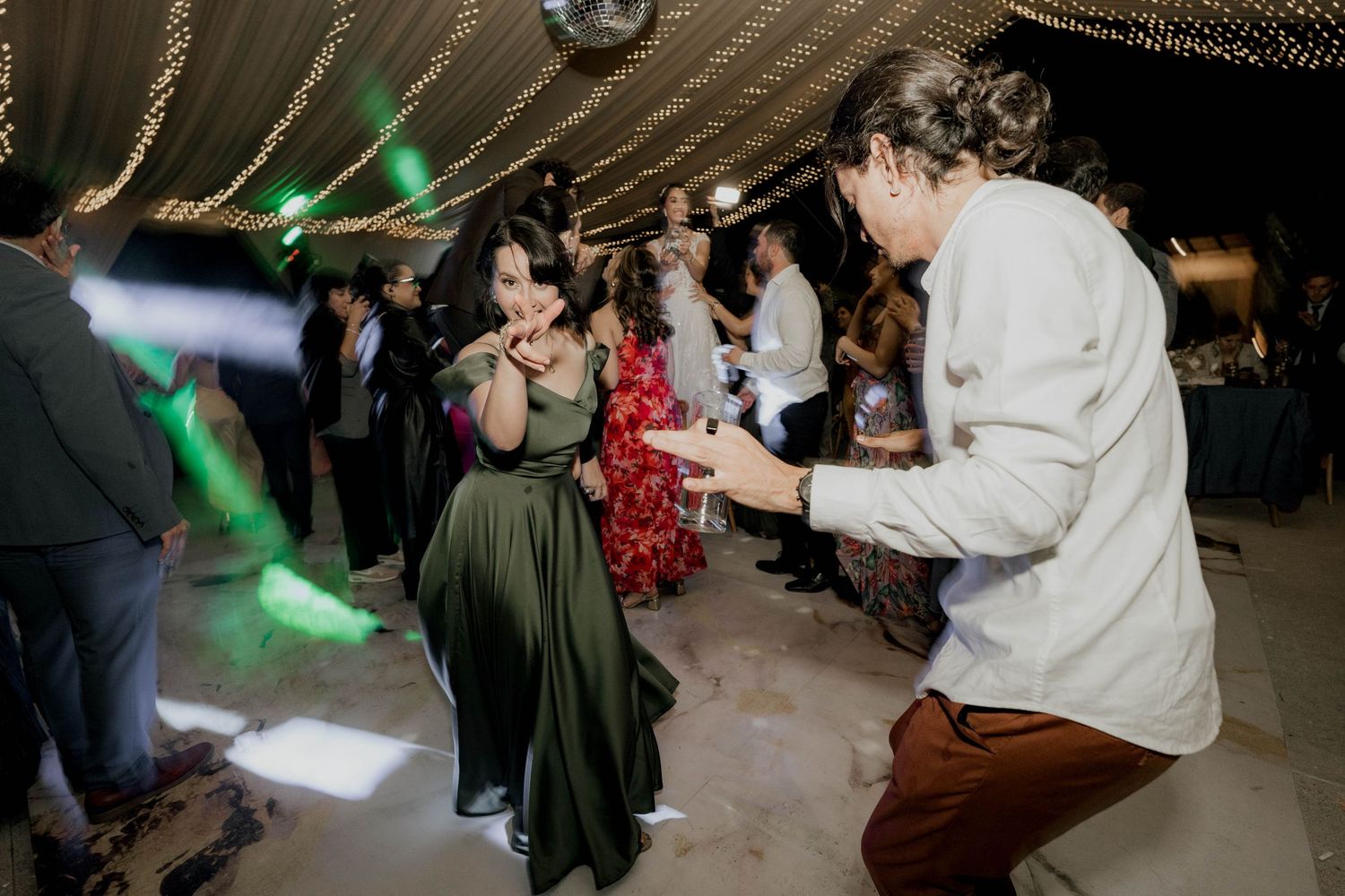 People dancing enthusiastically under green lighting at a wedding reception.