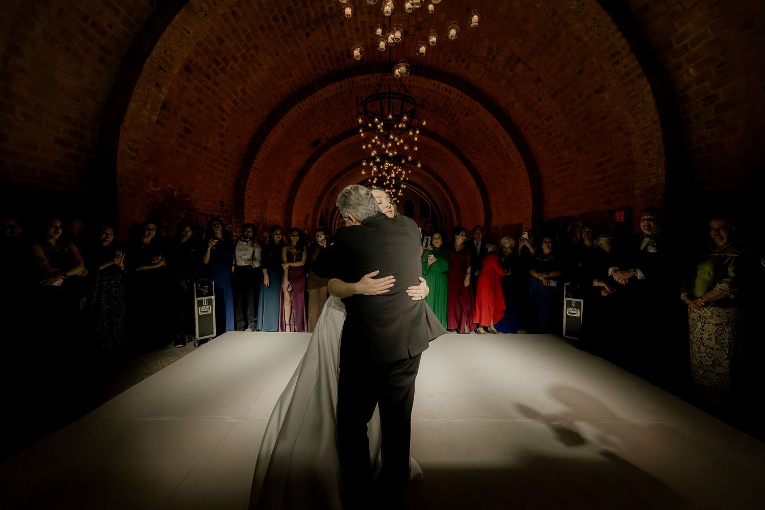 A couple shares their first dance in a beautifully lit brick archway venue.