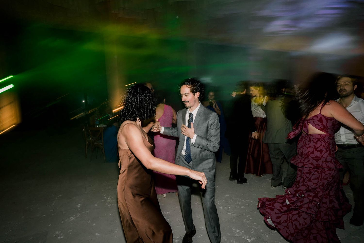 Couples dance together at an evening celebration with green ambient lighting.