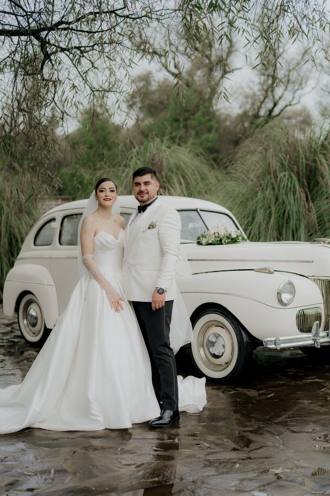 Wedding portraits featuring a classic white vintage car beside a pond with willow trees.