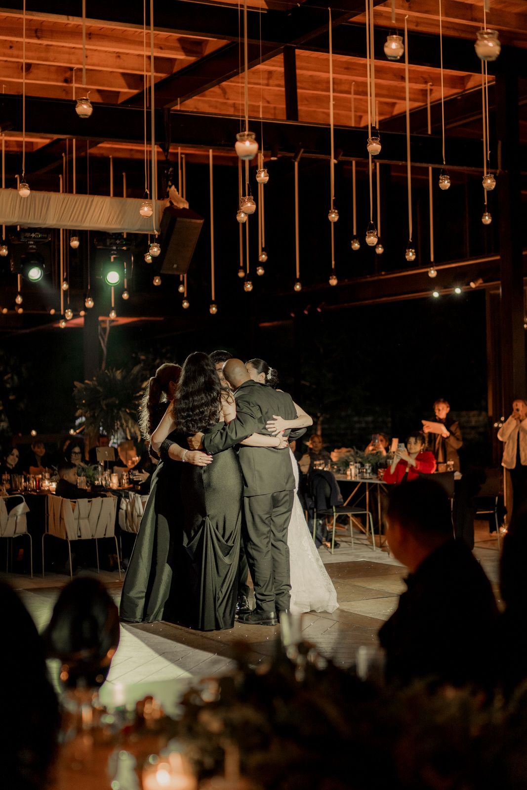 Wedding guests slow dancing under suspended lights at evening reception.