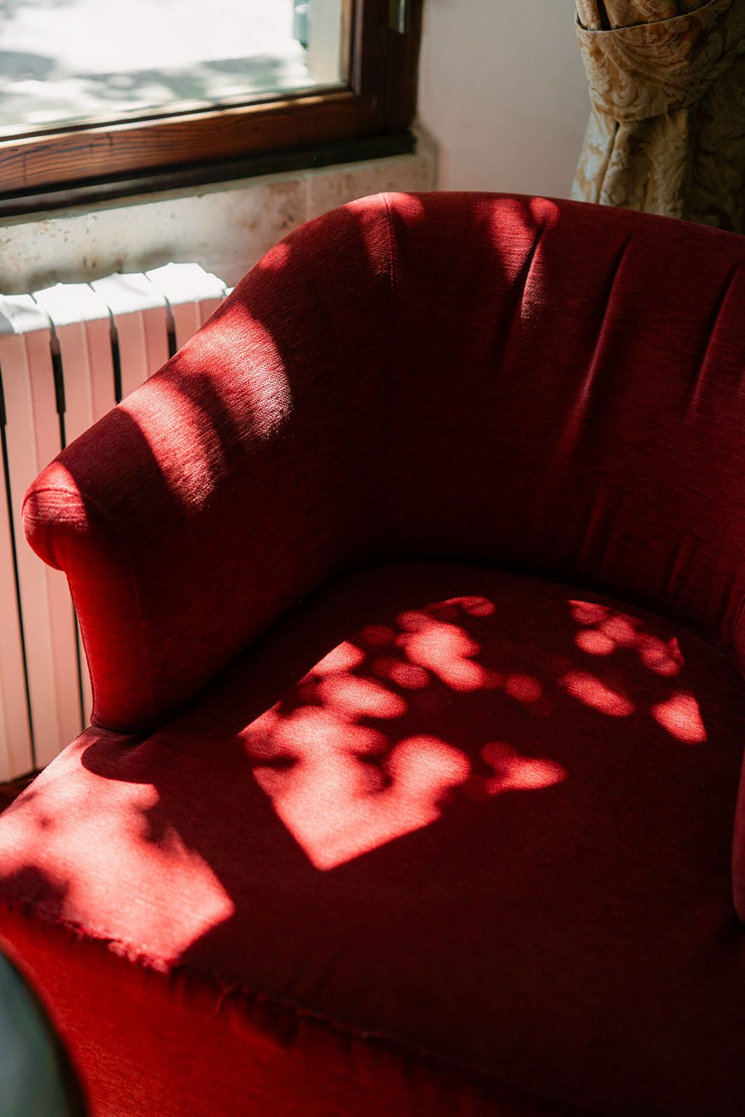 Sunlight casts heart-shaped shadows through window blinds onto a red couch cushion.