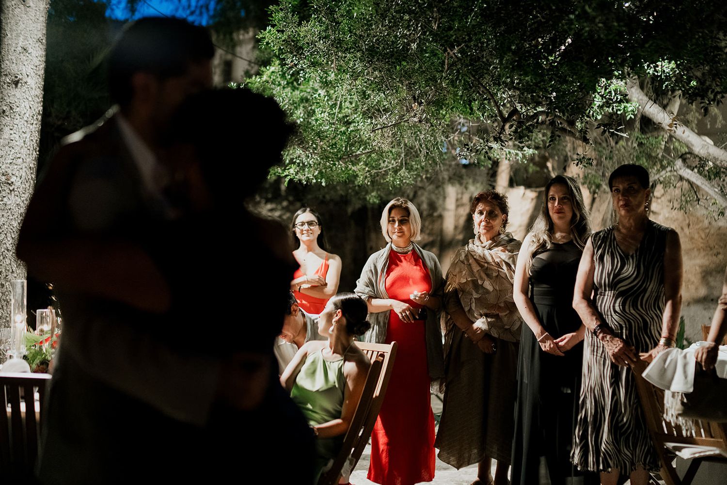 Wedding party members standing in line outdoors against a natural green backdrop during a ceremony.