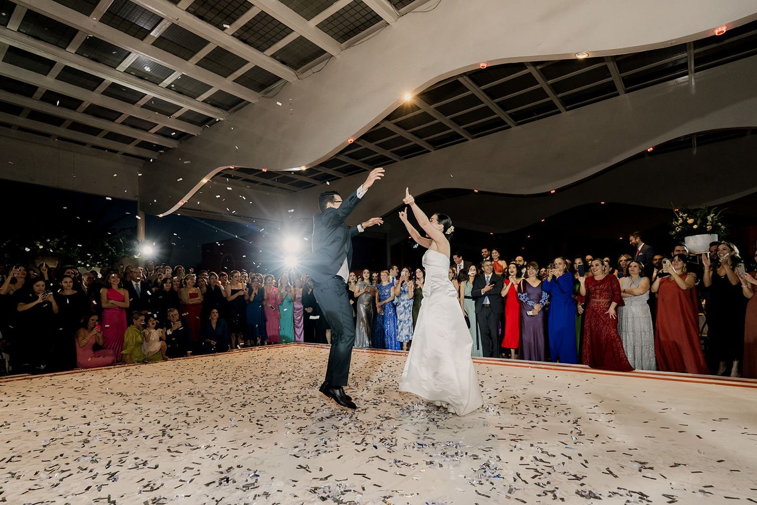 Bride and groom celebrate first dance with confetti falling around them before a large crowd of guests.