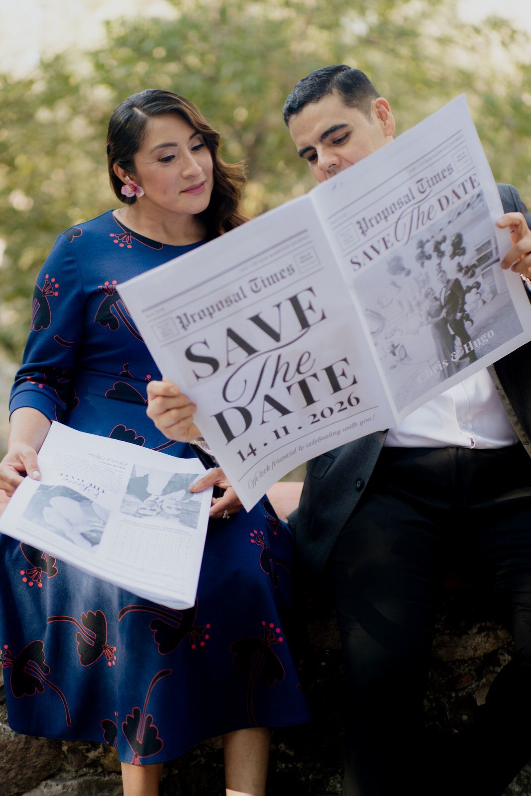 A couple shares laughter while reading save-the-date announcements together.