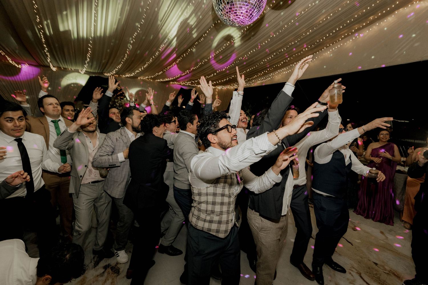 Wedding reception dance floor filled with guests celebrating under ambient lighting.
