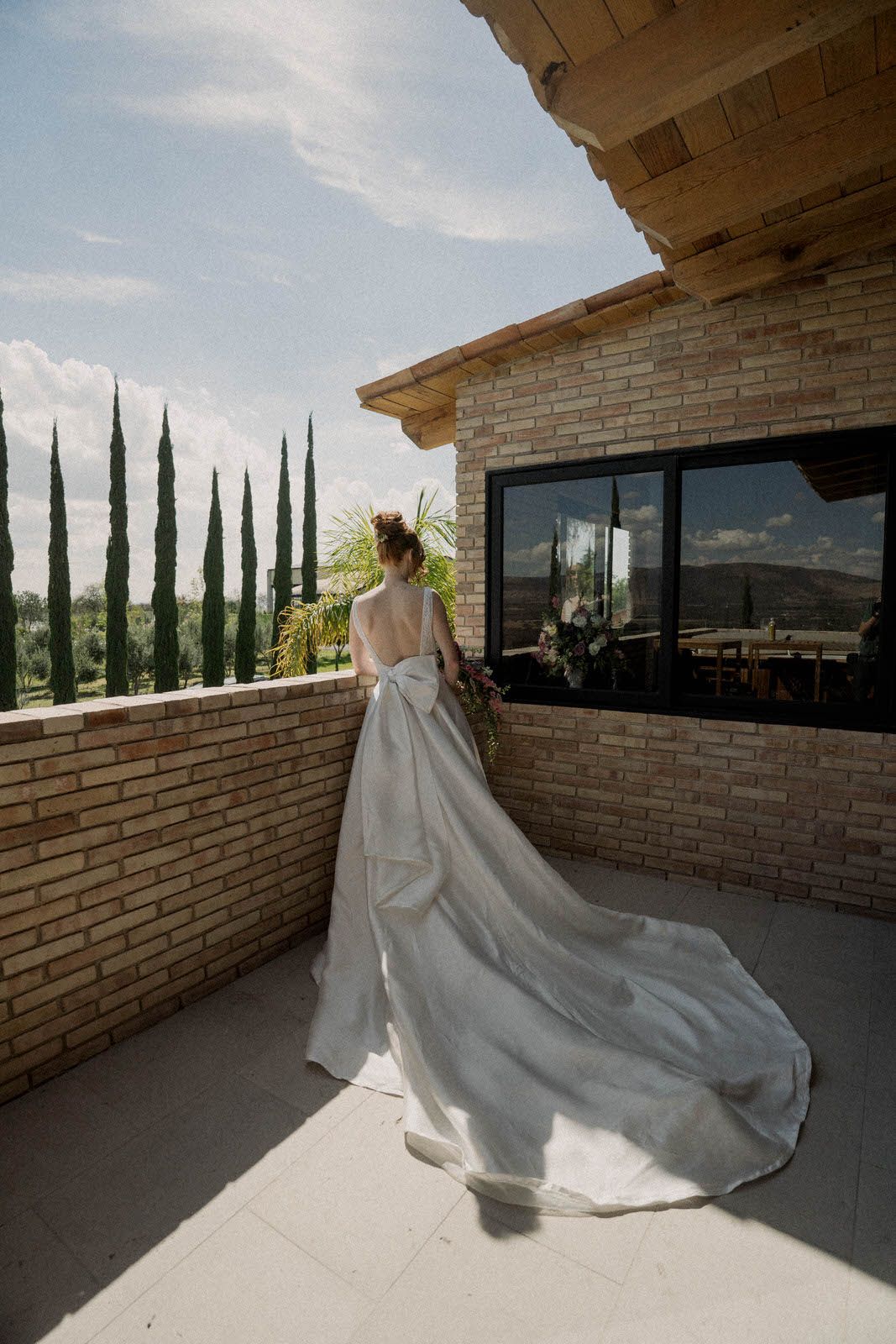Wedding dress with dramatic train flowing across patio with brick walls and mountain views.