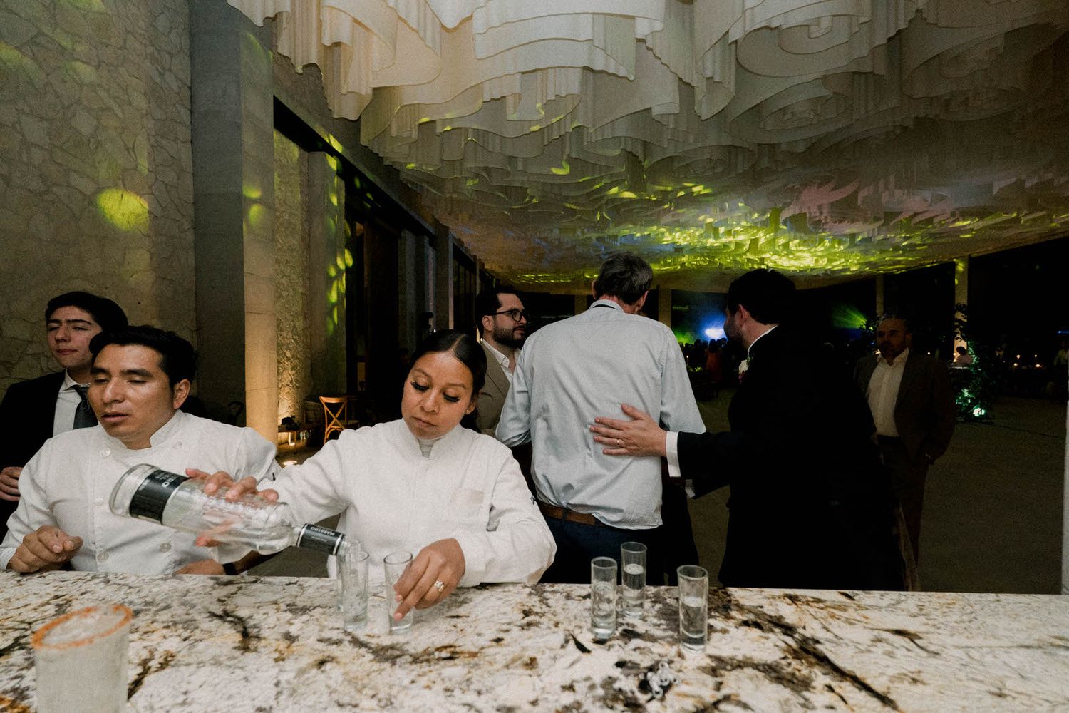 People in white shirts gather at a dimly lit venue with interesting architectural ceiling details.