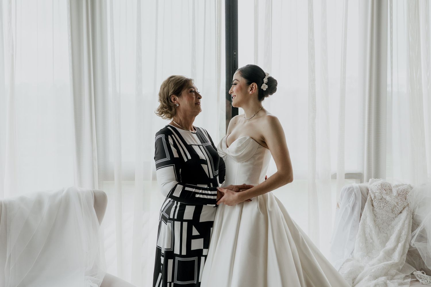 A tender moment during wedding dress fitting in a sunlit room.