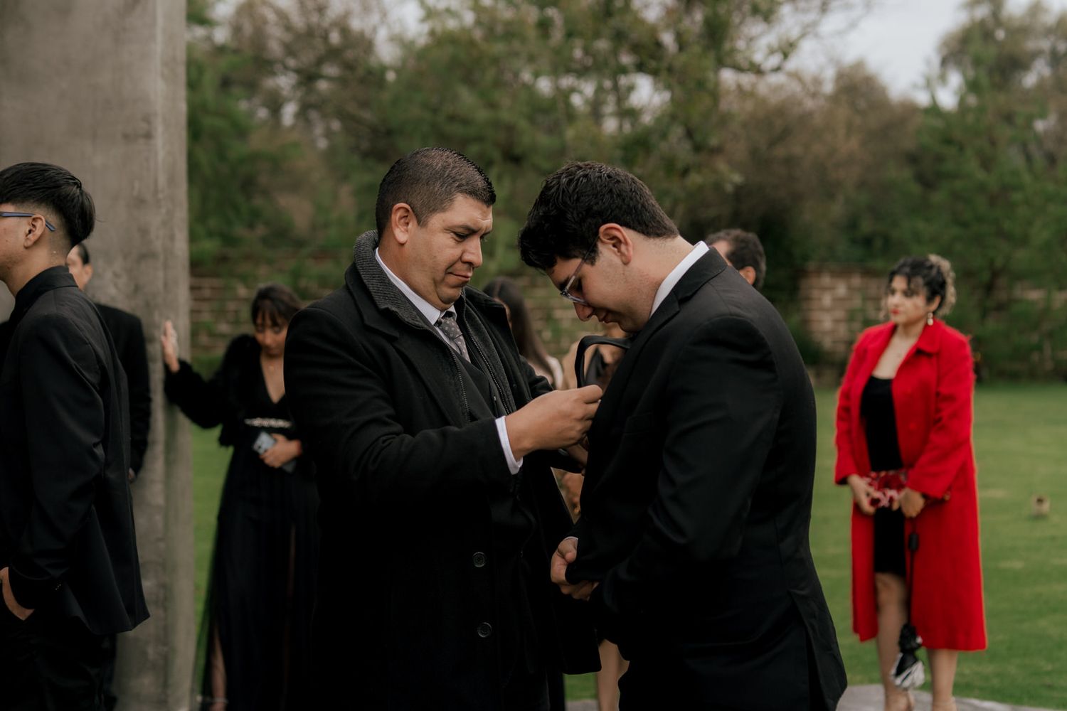 Two people share an intimate moment during a wedding ceremony outdoors with guests looking on.