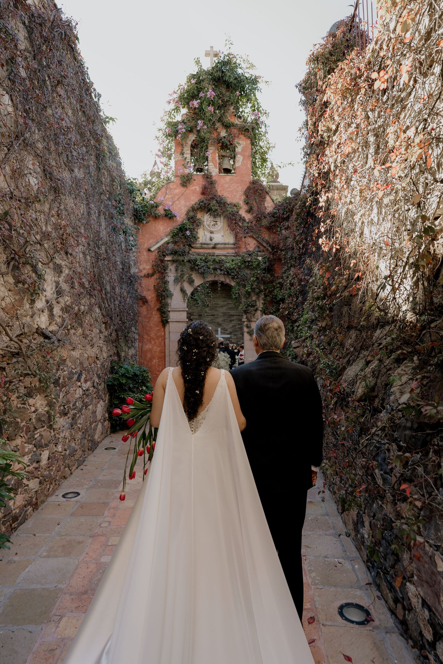 Couple walking through stone archway with climbing vines and flowers.