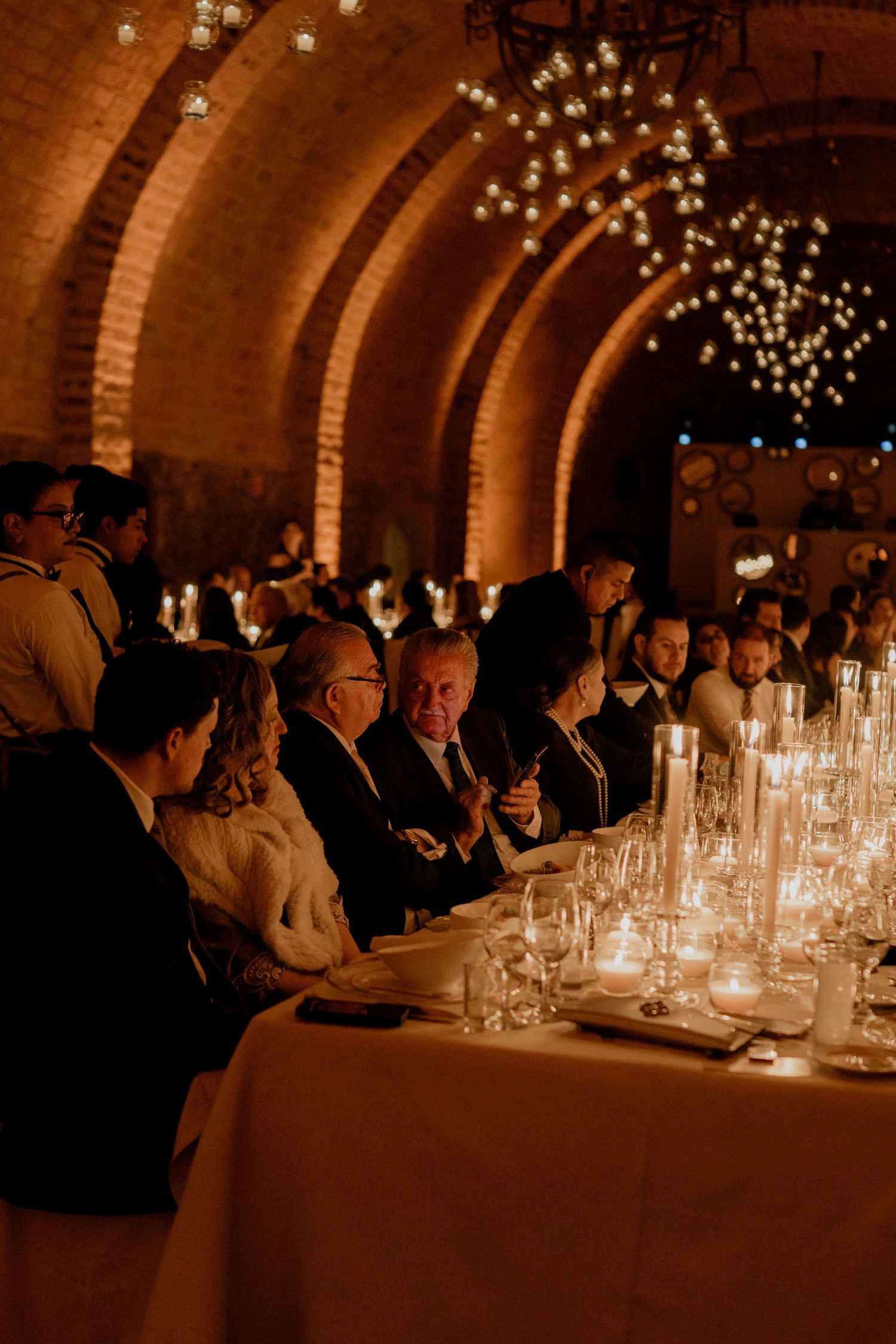 Wedding reception dinner in brick tunnel venue with guests seated at candlelit tables.