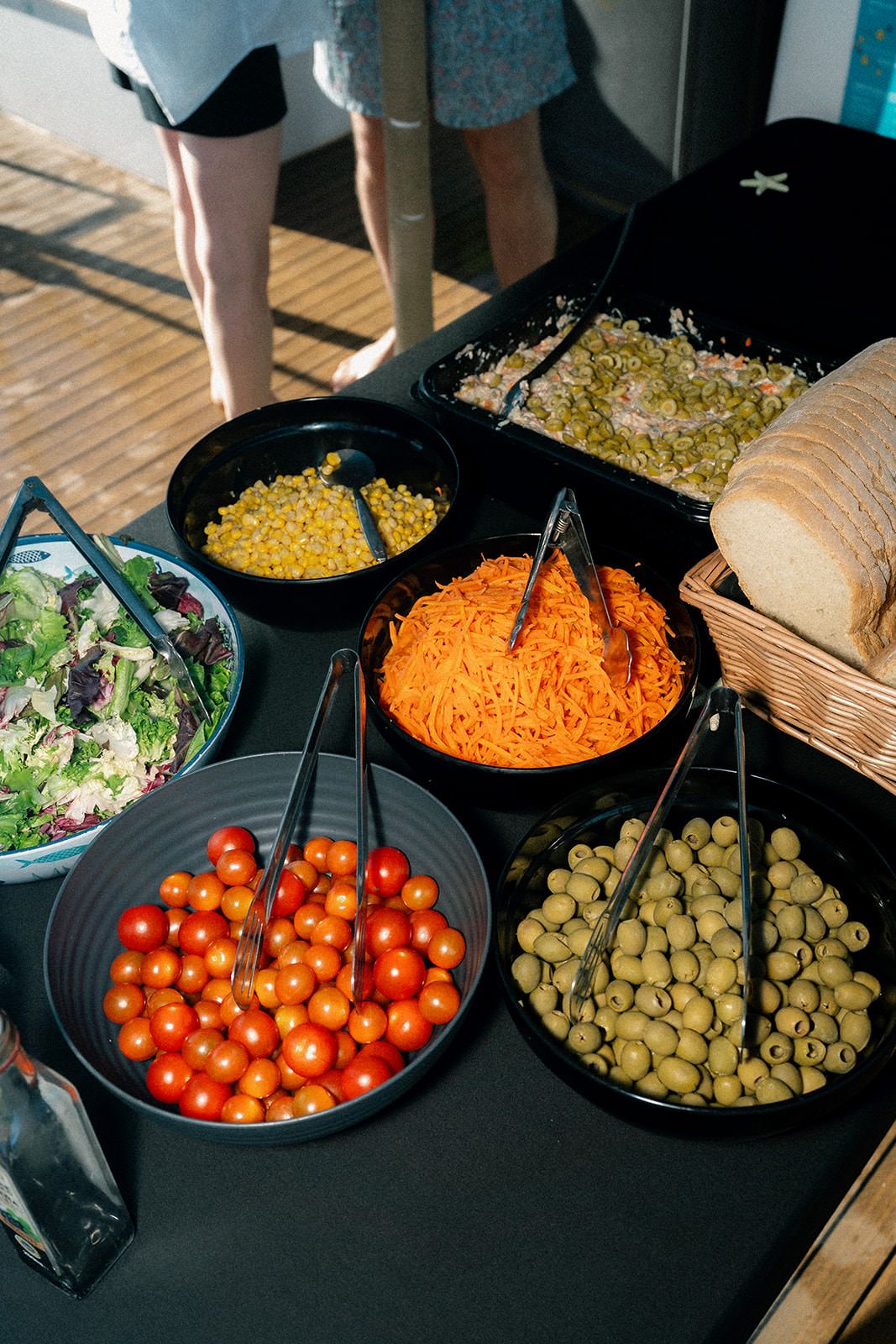 A buffet spread featuring black bowls filled with colorful ingredients including cherry tomatoes, olives, and shredded carrots.