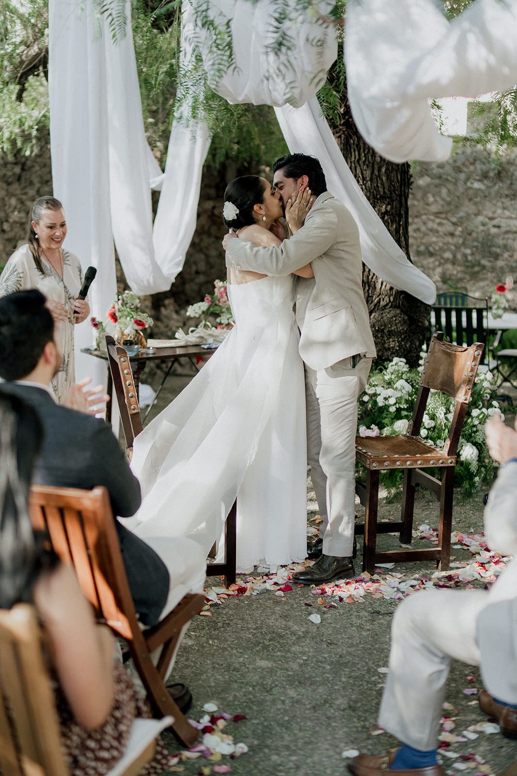 White flowing fabric creates an ethereal atmosphere at an outdoor wedding ceremony with rose petals scattered on grass.