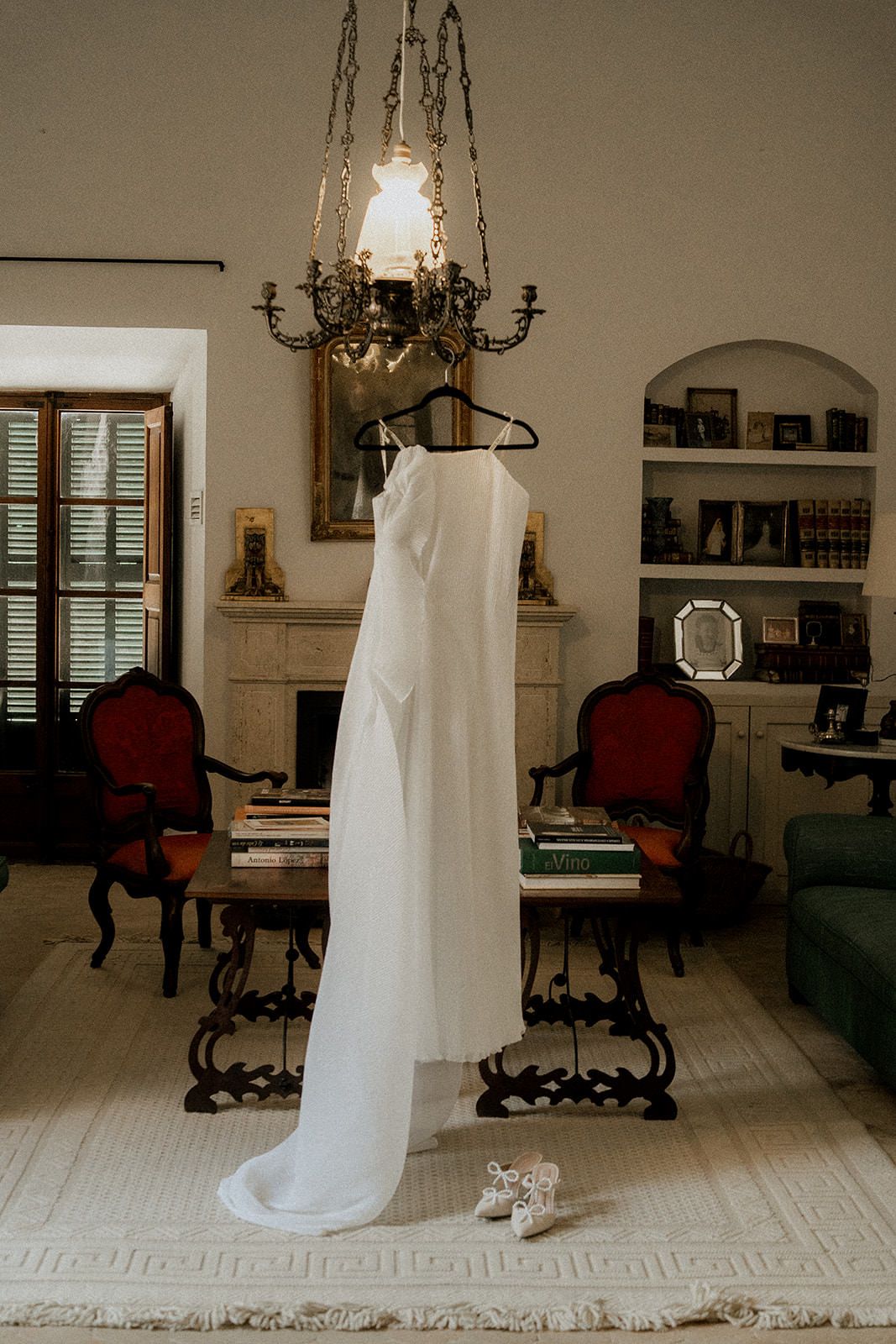 Wedding dress displayed in a traditional room with antique furniture and a chandelier.
