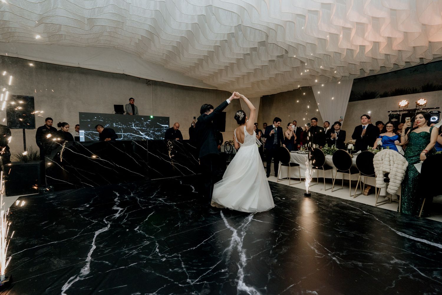 Bride and groom share first dance on marble floor at elegant wedding reception.