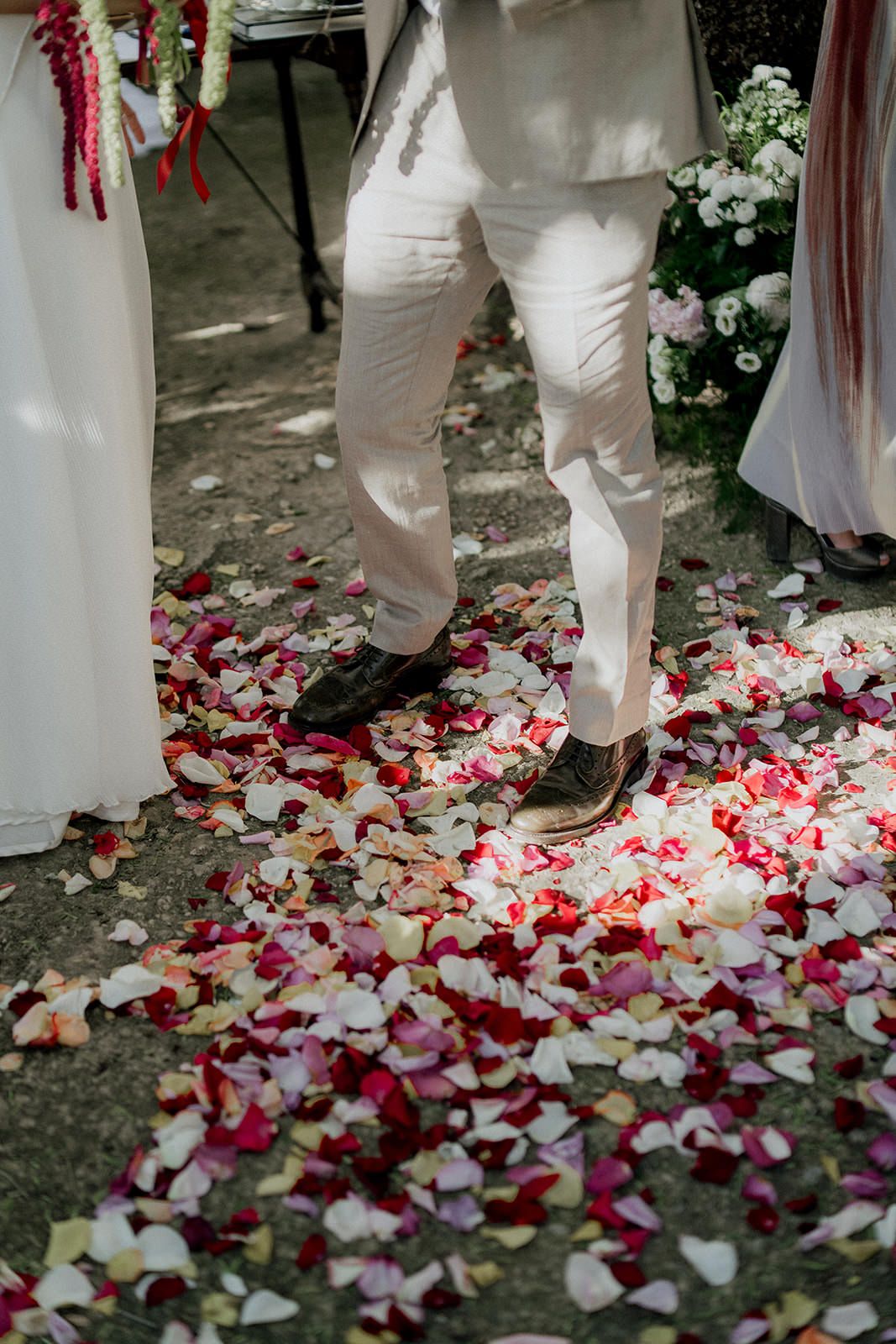 Rose petals scattered on the ground with people wearing white clothing standing above them.